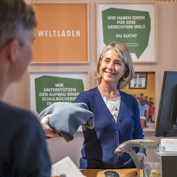 Weltladen-Mitarbeiterin verkauft einer Kundin Fair Fashion